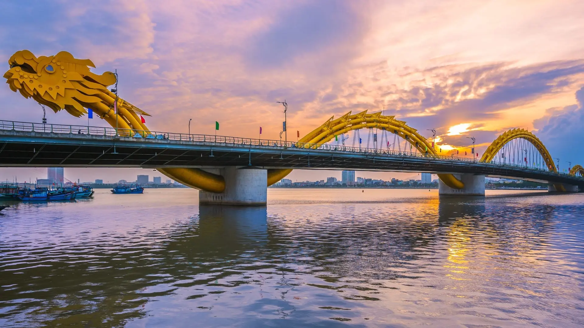 Dragon Bridge in Da Nang viewed from a distance at sunset, stretching across the Han River with golden dragon design and city skyline