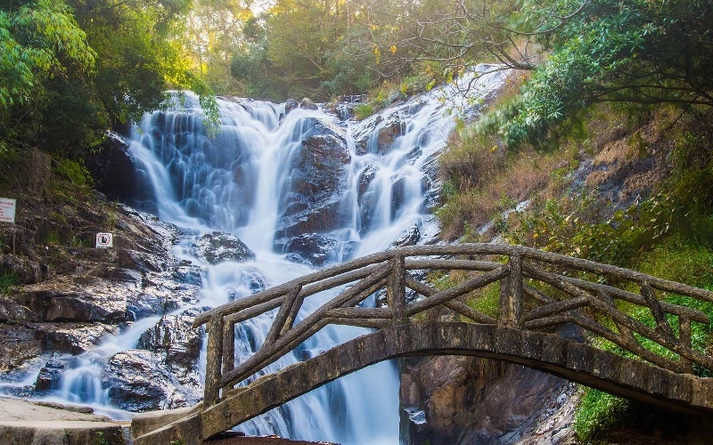 Datanla Waterfall cascading over rocky cliffs with a wooden bridge in Da Lat, Vietnam.