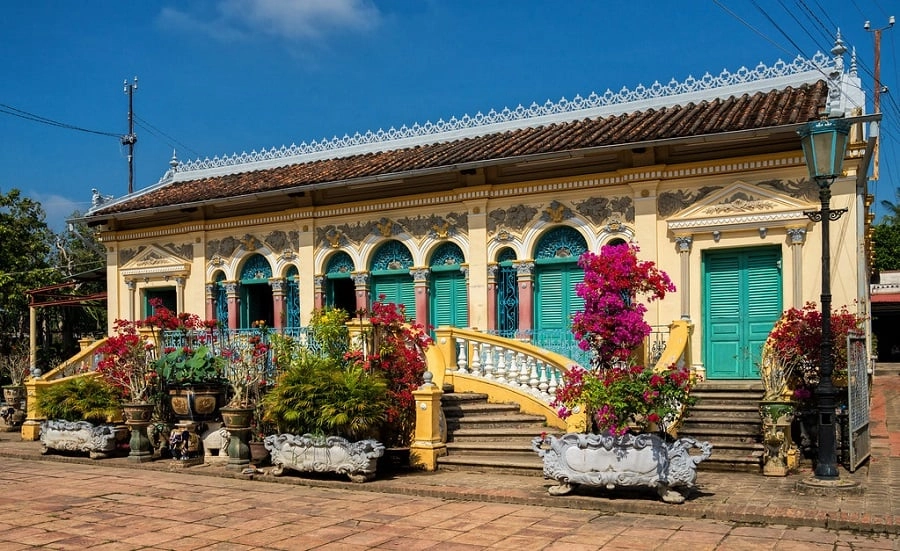 Binh Thuy Ancient House with yellow façade, green shutters, and blooming flowers in Can Tho.
