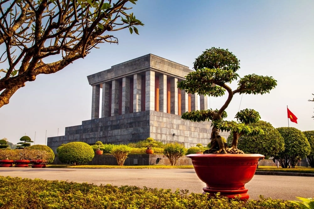 Ho Chi Minh Mausoleum in Hanoi surrounded by manicured gardens and a Vietnamese flag.