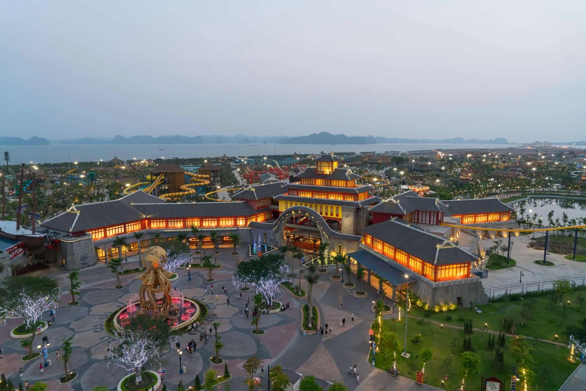 Sun World Ha Long Park at sunset with illuminated buildings, amusement rides, and coastal cityscape.
