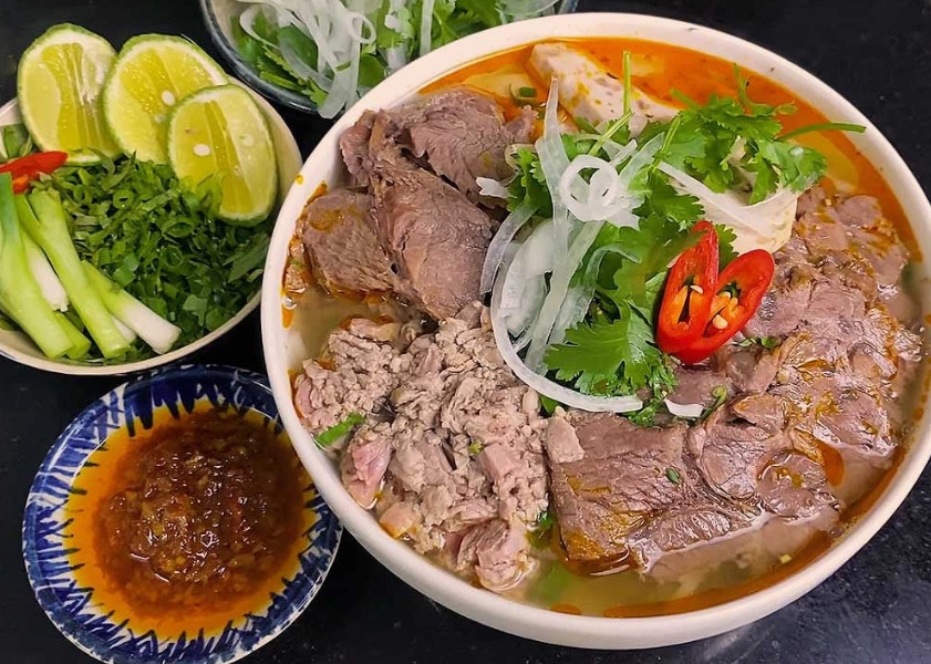 A bowl of authentic Bun Bo Hue Vietnamese spicy beef noodle soup with herbs and lime