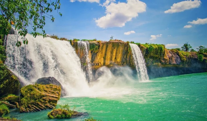 Panoramic view of Dray Nur Waterfall cascading over rocky cliffs into emerald water.