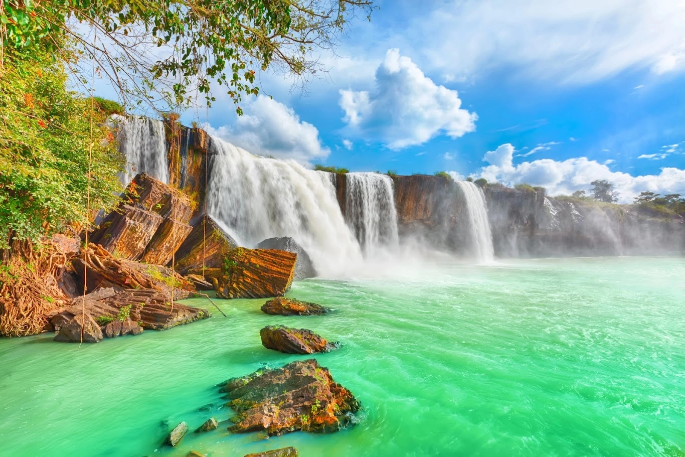 Powerful cascade of Dray Nur Waterfall flowing into turquoise water surrounded by rocky cliffs.