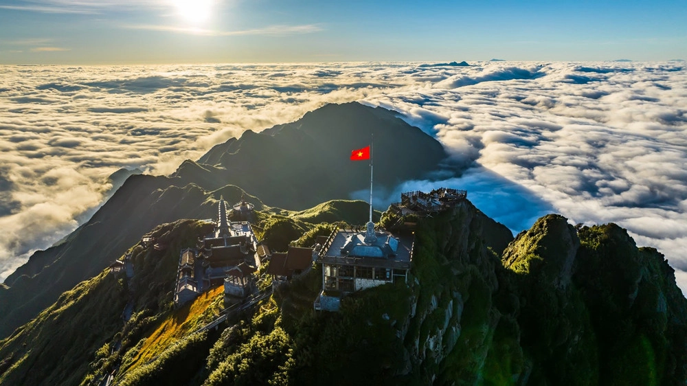 Vietnamese flag waving at Fansipan Peak above a sea of clouds.