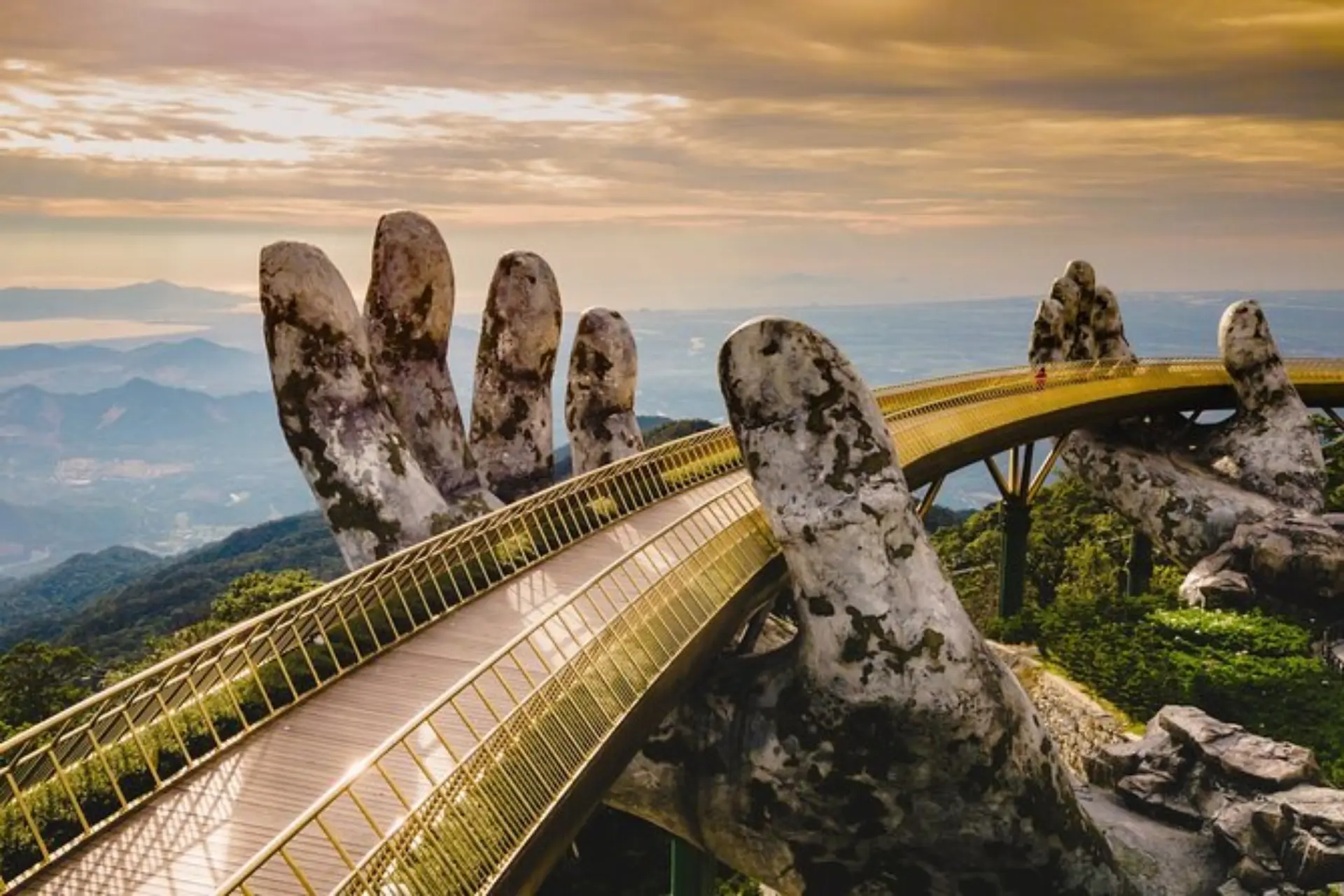 The iconic Golden Bridge Ba Na Hills supported by giant stone hands overlooking mountains.