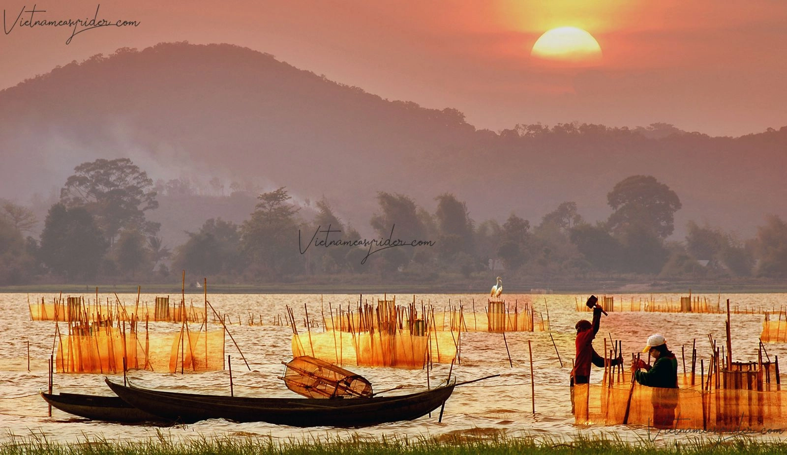 Traditional fishing boats and nets at sunset on Lak Lake with mountains in the background.