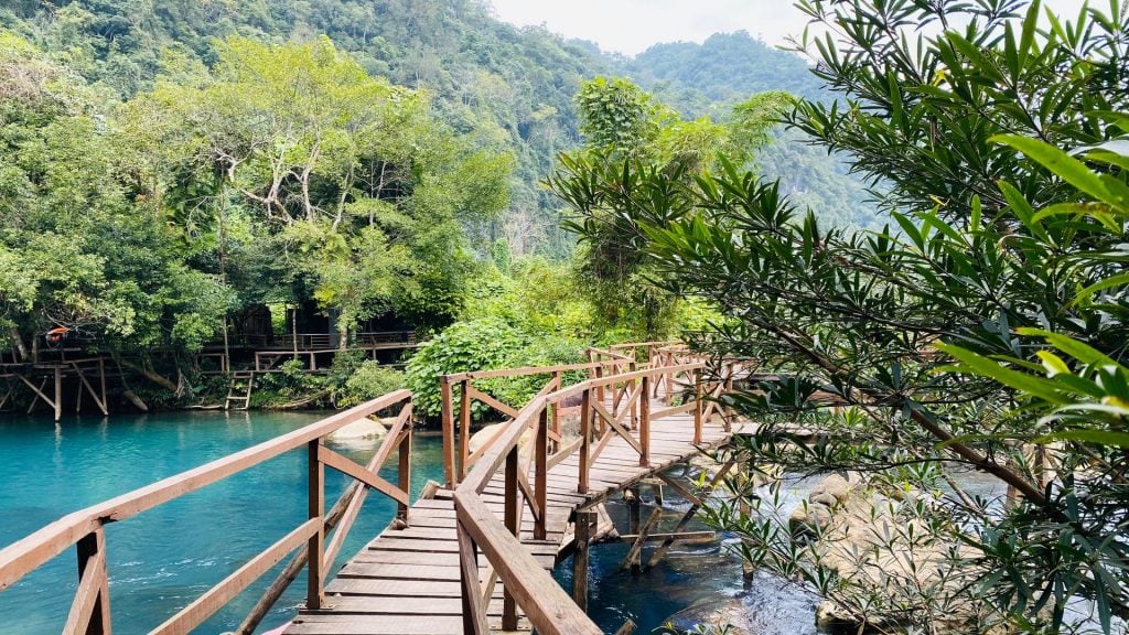 Wooden bridge over turquoise water at Mooc Spring surrounded by jungle