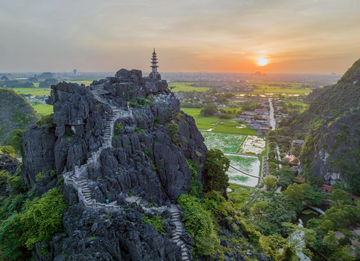 Panoramic view from Mua Cave with stone steps leading to a mountain peak overlooking rice fields at sunset
