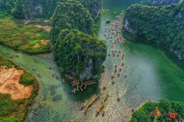 Aerial view of Ninh Binh landscape with rivers, limestone mountains, and boats winding through green valleys.