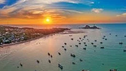 Sunset over Phan Thiet Beach with fishing boats scattered across calm turquoise waters in Vietnam.