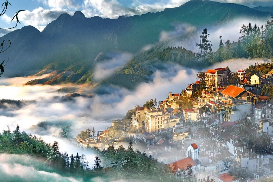 Sapa town with red-roofed buildings surrounded by mountains and mist.