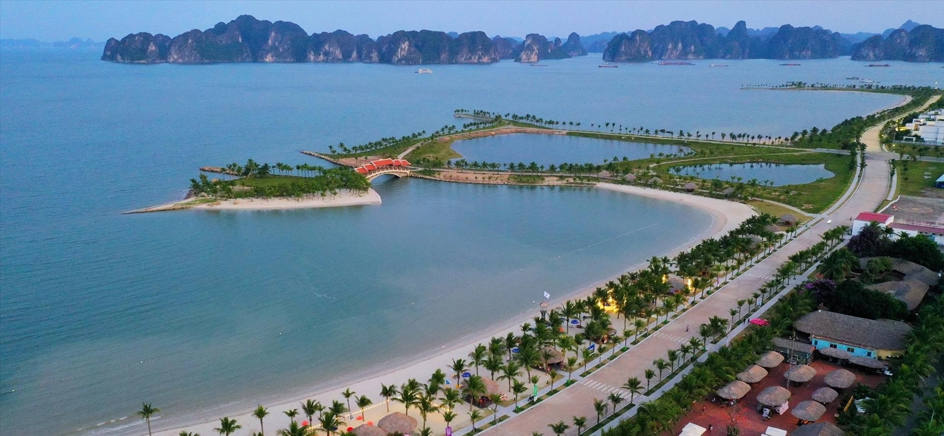 Aerial view of Tuan Chau Island with sandy beach, palm-lined promenade, and calm turquoise waters in Ha Long Bay.