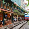 Visitors enjoying Hanoi Train Street cafés as a train passes through the narrow railway lined with restaurants and greenery with StarTour