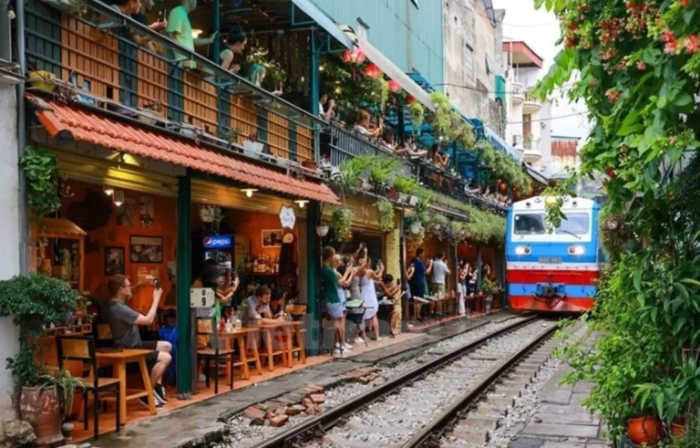 Visitors enjoying Hanoi Train Street cafés as a train passes through the narrow railway lined with restaurants and greenery with StarTour