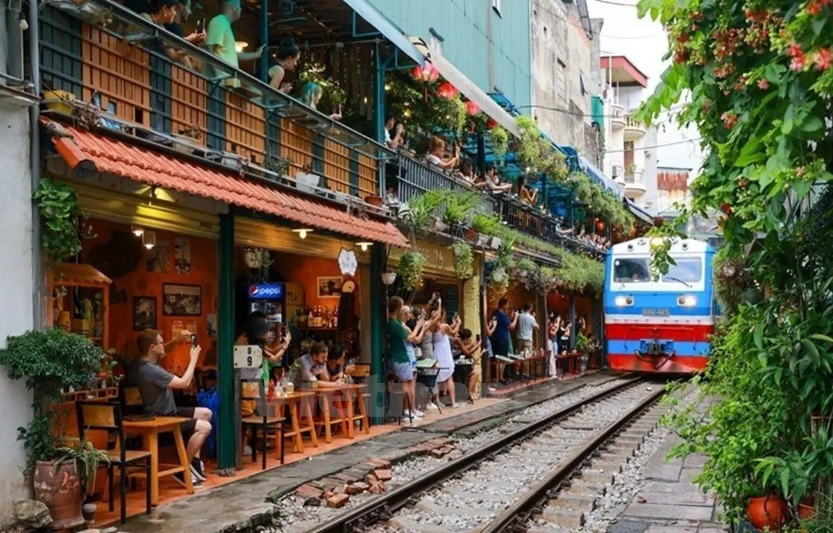 Visitors enjoying Hanoi Train Street cafés as a train passes through the narrow railway lined with restaurants and greenery with StarTour
