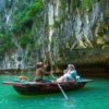 Visitors enjoying a traditional boat ride on emerald water near limestone cliffs and cave formations at Luon Cave in Ha Long Bay with StarTour