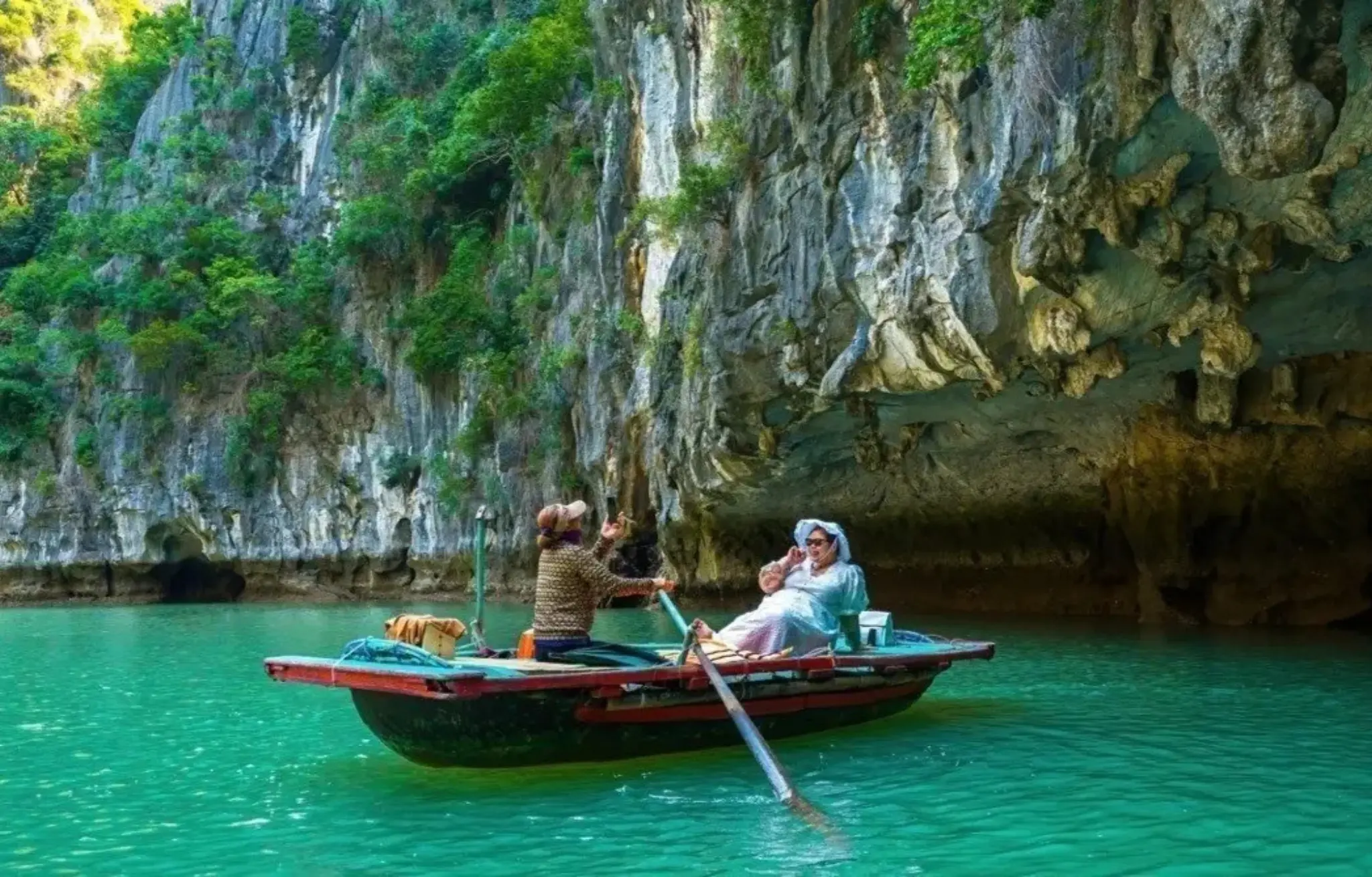 Visitors enjoying a traditional boat ride on emerald water near limestone cliffs and cave formations at Luon Cave in Ha Long Bay with StarTour