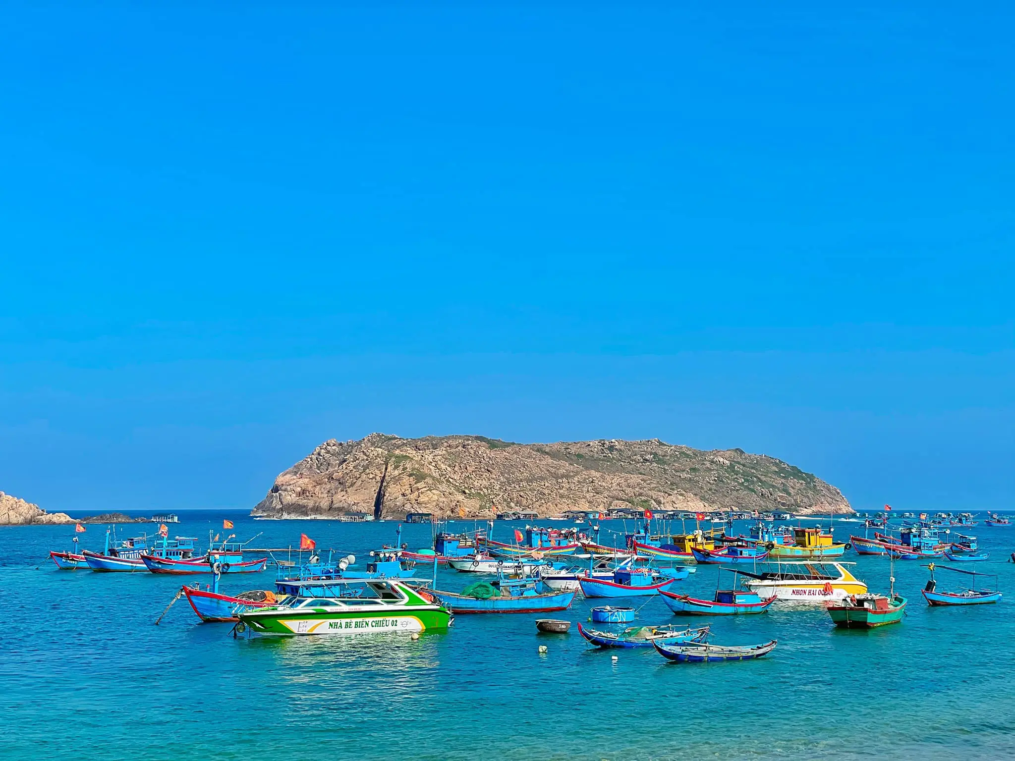 Colorful fishing boats on clear blue sea near a rocky island in Vietnam by Startour