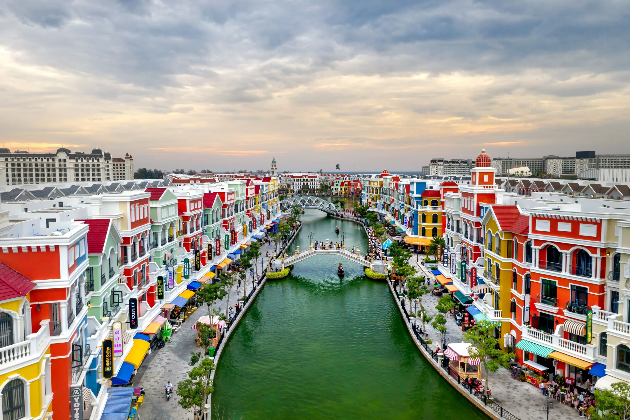 A panoramic view of Grand World in Phu Quoc Vietnam featuring colorful European-style buildings, a scenic canal, pedestrian bridges, and vibrant waterfront attractions at sunset.