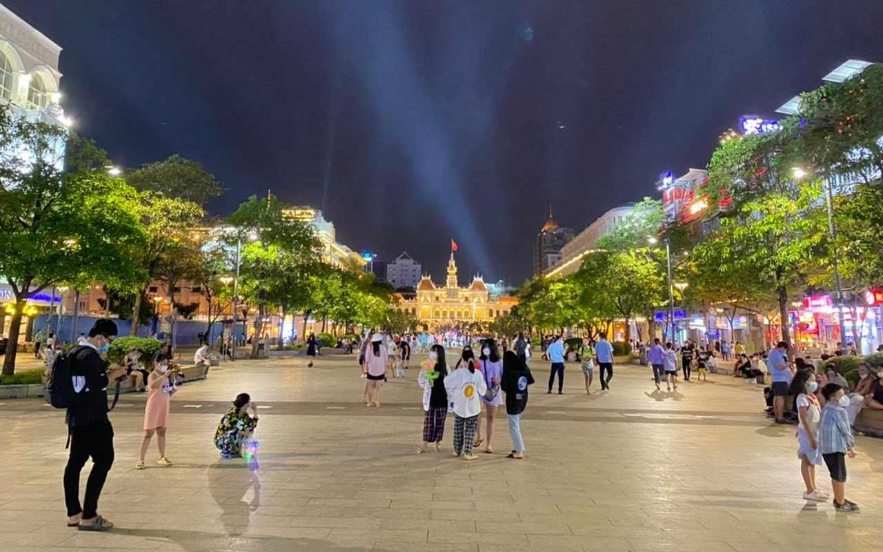 Crowd of people and tourists enjoying nightlife at Nguyen Hue Walking Street with the illuminated Ho Chi Minh City People's Committee Building in the background
