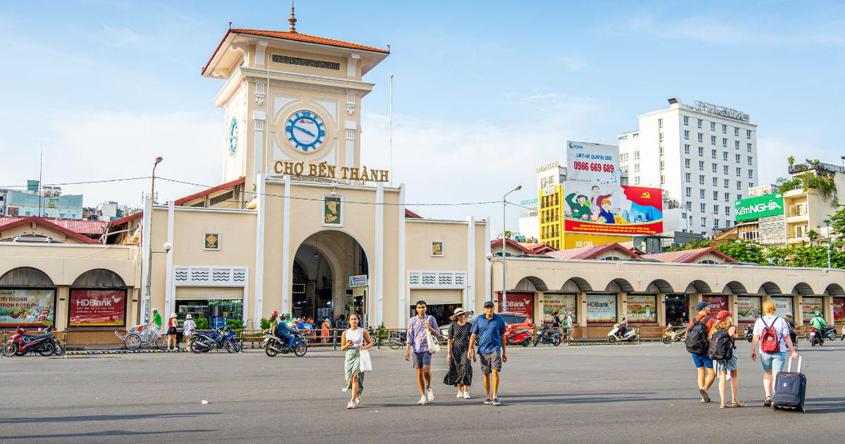 The iconic clock tower facade of Ben Thanh Market in District 1, Ho Chi Minh City, with tourists walking in the foreground during daytime.