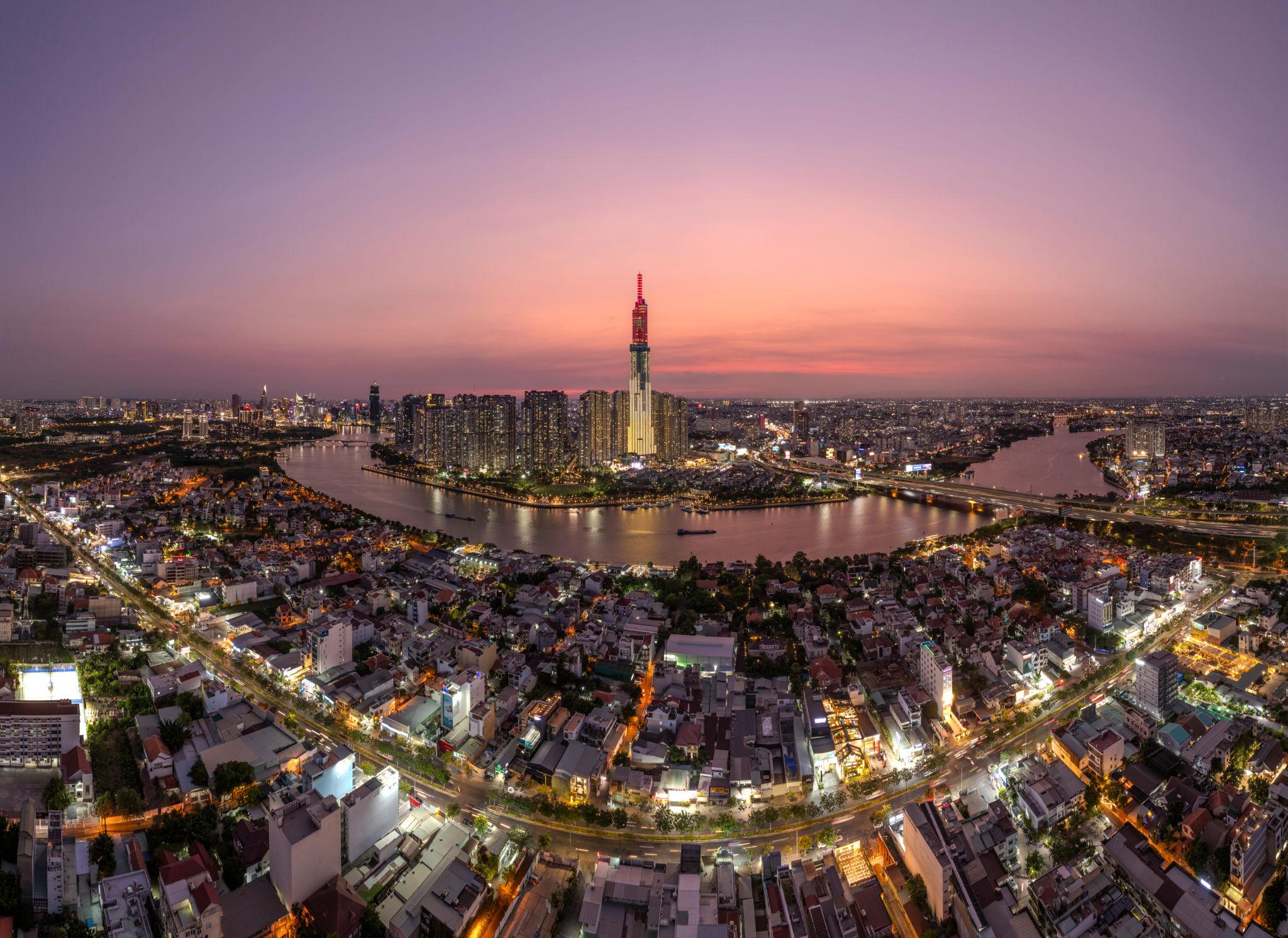 Panoramic aerial view of the Ho Chi Minh City skyline at sunset, featuring the iconic Landmark 81 skyscraper rising above the Saigon River loop.
