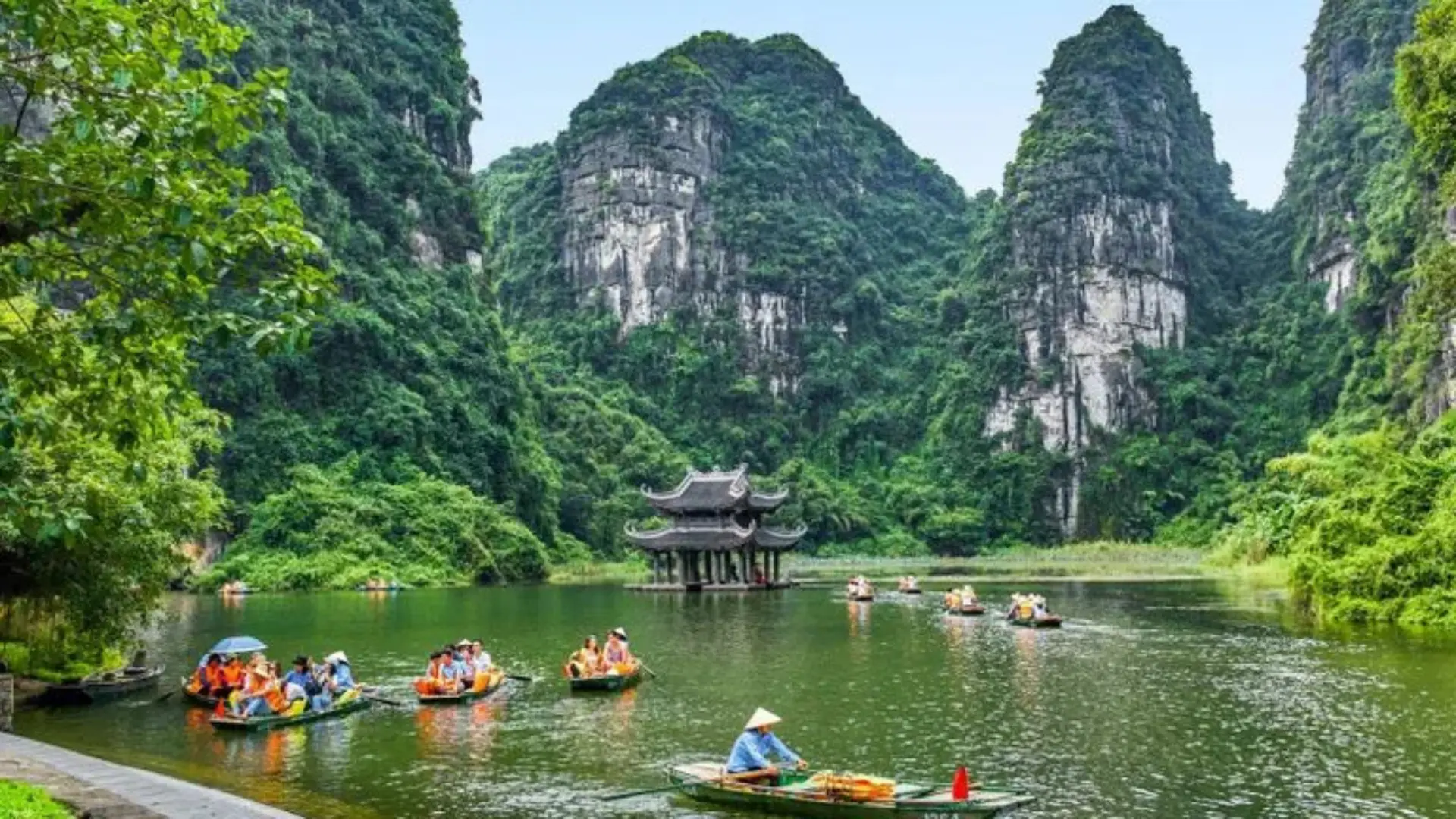 Visitors enjoying a traditional boat tour through the limestone karst mountains and tranquil waterways of Trang An Landscape Complex in Ninh Binh, Vietnam, a UNESCO World Heritage Site.